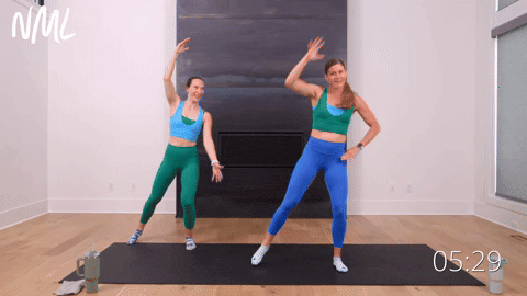 two women performing a standing oblique crunch and inner heel tap in a quick standing ab workout