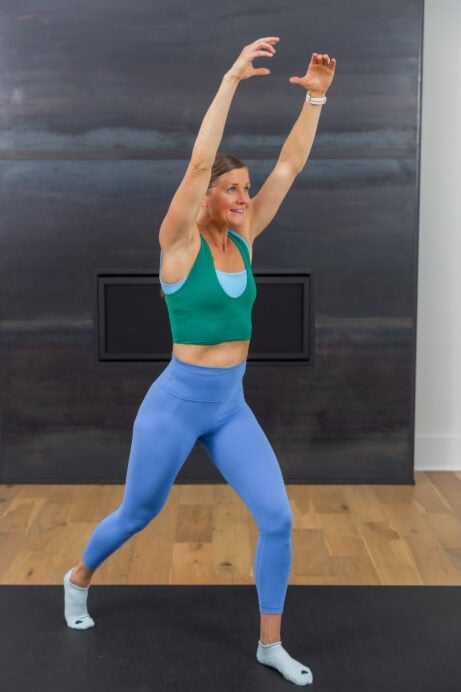 woman with her arms raised overhead preparing to perform a straight leg kick in a quick ab workout