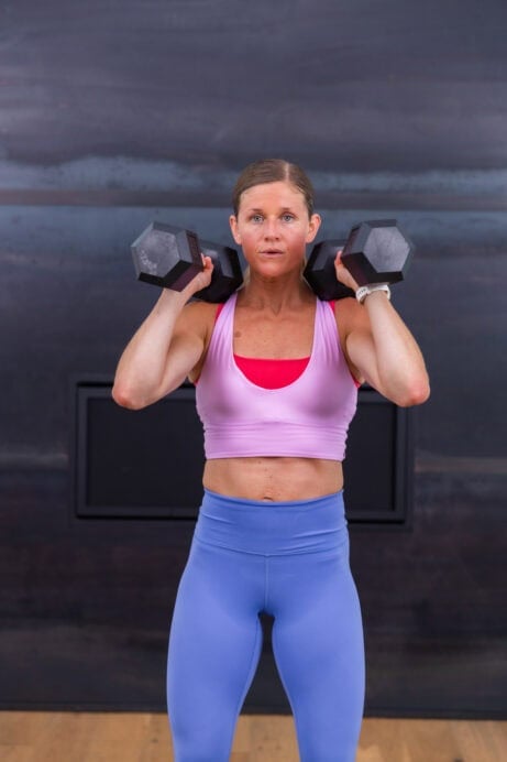 woman holding dumbbells racked at her shoulders in a hiit workout routine