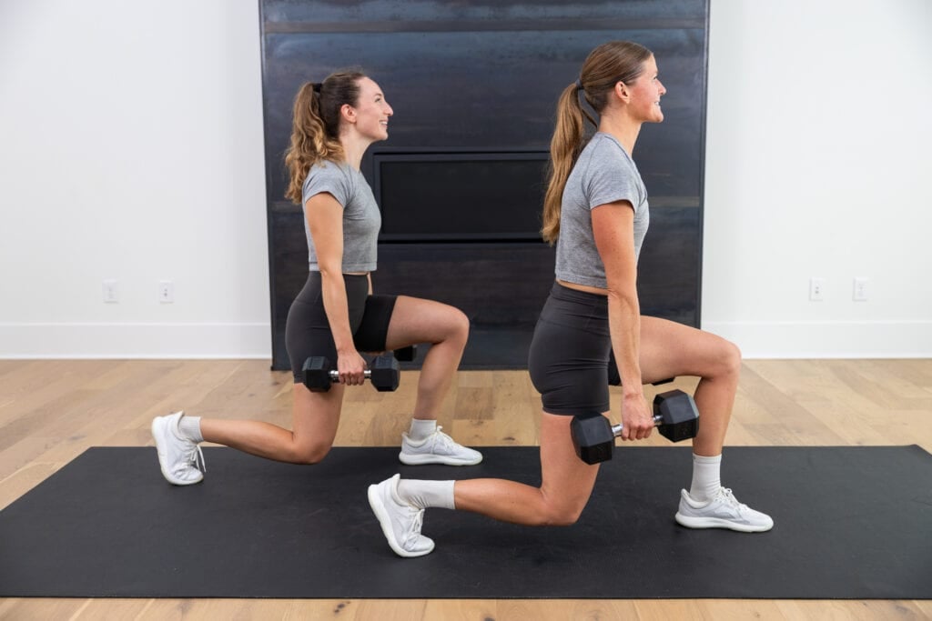 two women performing a lunge hold with dumbbells in a squat workout. as part of lunge and squat alternatives for bad knees. 